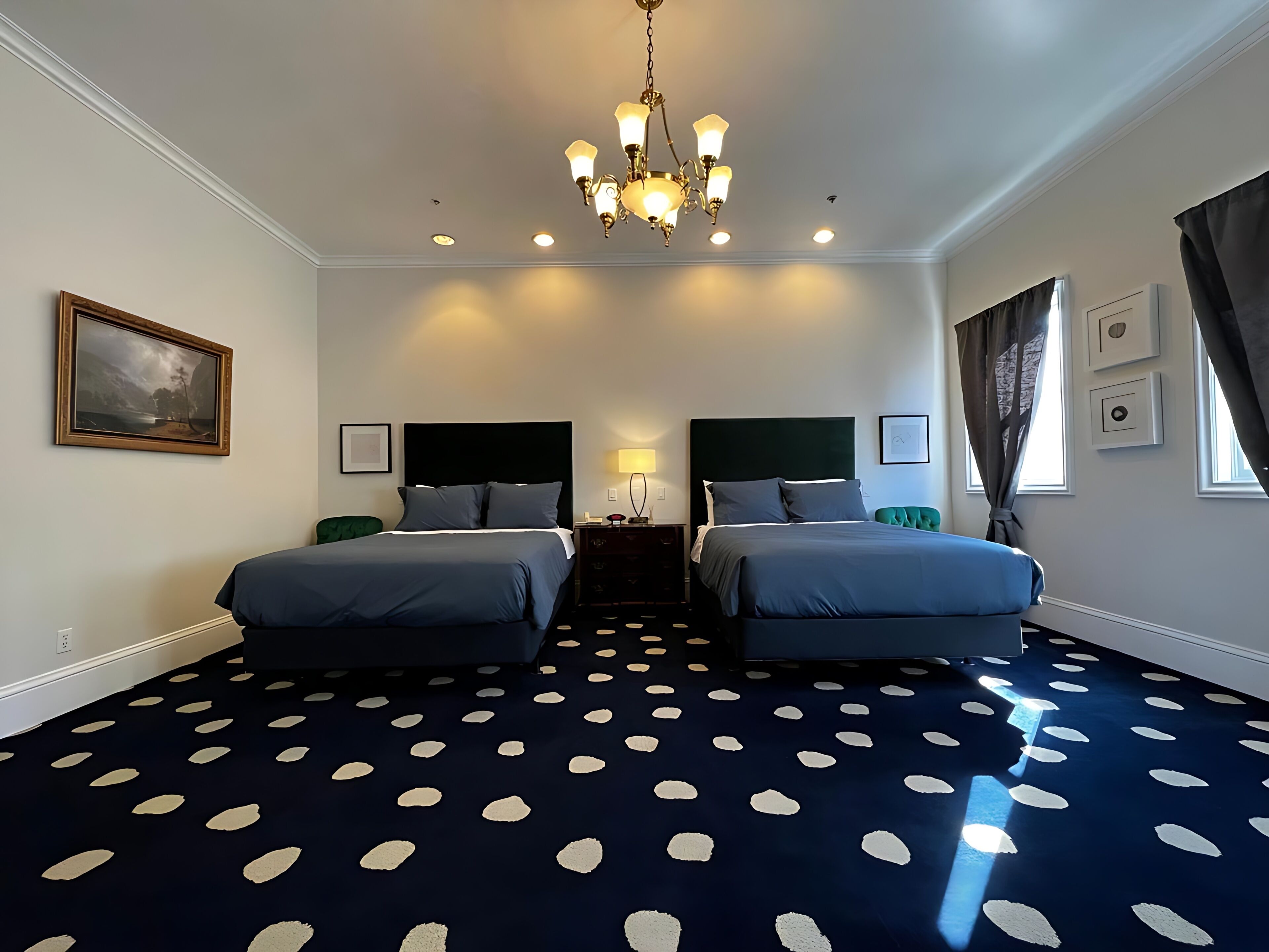 Habitación de hotel con dos camas, una araña, un cuadro y una alfombra de lunares.
