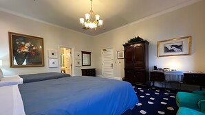 Hotelkamer met een groot bed, een bureau met een computer, een stoel, een kast en een deur naar een andere kamer.