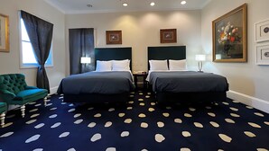 Een hotelkamer met twee bedden, een kroonluchter, een groene fauteuil en een gekleurd tapijt met stippen.