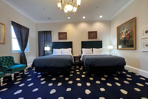 Habitación de hotel con dos camas, un candelabro, un sillón verde y una alfombra de lunares.