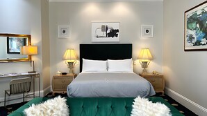 Et hotelværelse med en stor seng, to sengeborde med lamper, et skrivebord med stol, et spejl og kunst på væggene.