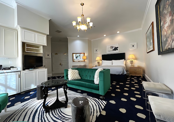 A hotel room with a green sofa, a round coffee table, a TV, a bed with white bedding, and a chandelier. - Premium King Grand Suite Near Sacramento's Top Attractions (Sacramento)