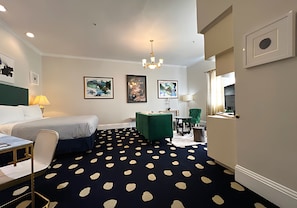 A hotel room with a bed, desk, chair, green armchair, and a patterned carpet. - Premium King Grand Suite Near Sacramento's Top Attractions (Sacramento)