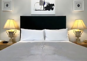 A hotel room with a large bed, two bedside lamps, a black headboard, and abstract wall art. - Premium King Grand Suite Near Sacramento's Top Attractions (Sacramento)