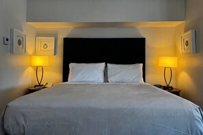 A hotel room with a large bed, two bedside lamps, a black headboard, and framed pictures on the walls. - Elegant King Junior Suite at The Sterling Hotel Sacramento (Sacramento)
