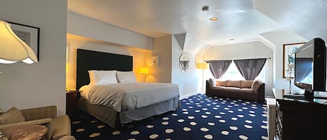 Habitación de hotel con cama, sofá, televisor y alfombra estampada.