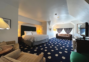 Quarto de hotel com cama, sofá, televisão e carpete estampado.