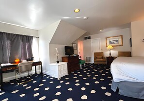 A hotel room with a bed, a desk with a chair, a dresser, a television, and a patterned carpet. - Elegant King Junior Suite at The Sterling Hotel Sacramento (Sacramento)