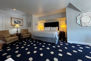 A hotel room with a bed, two armchairs, a small table, and a patterned carpet. - Elegant King Junior Suite at The Sterling Hotel Sacramento (Sacramento)