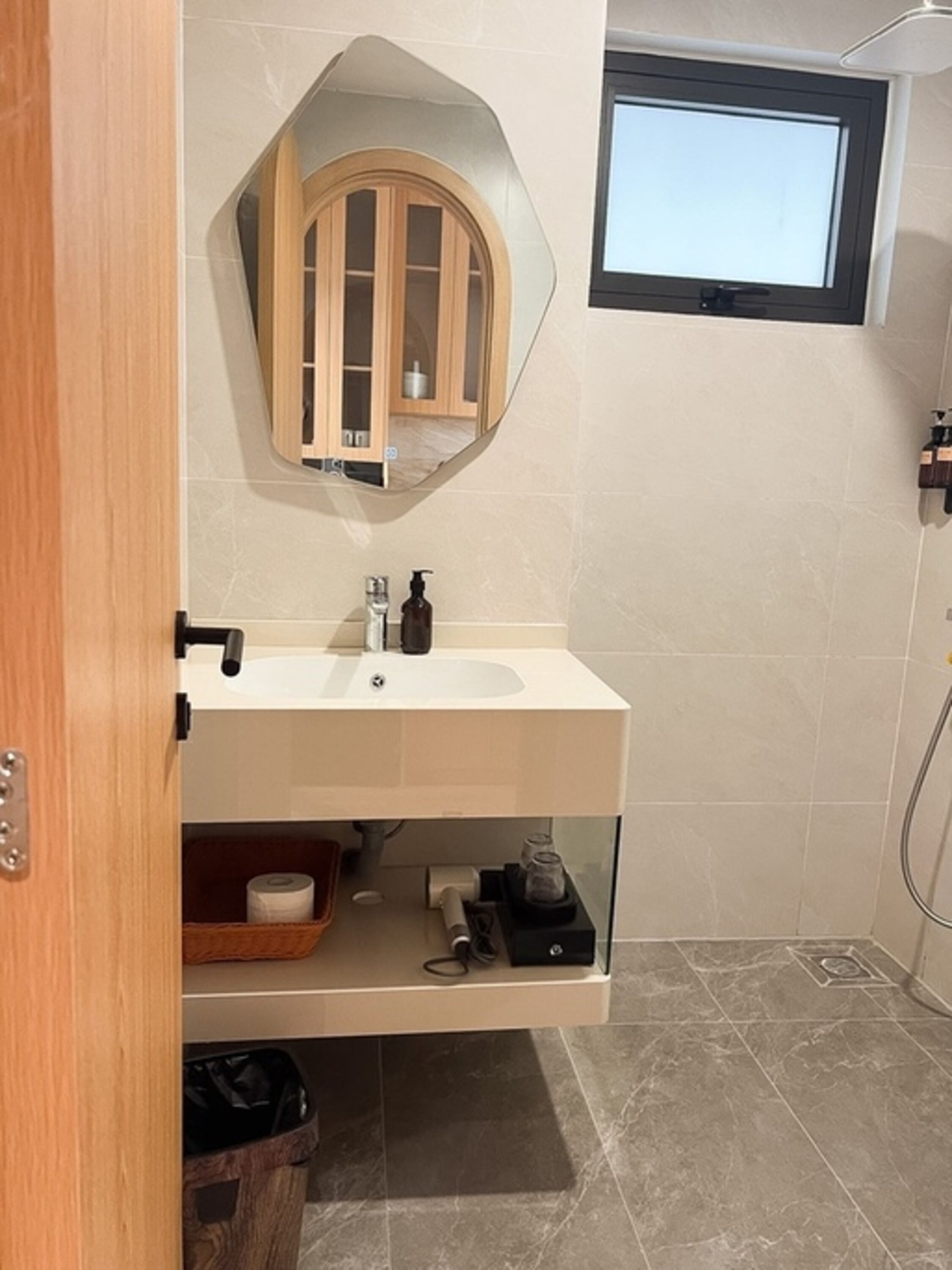 Ein Badezimmer mit einem weißen Waschbecken, einem Holzschrank, einem Spiegel und einem Fenster.
