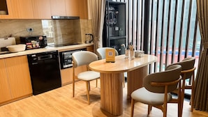 A modern kitchen with wooden cabinets, a dishwasher, a coffee machine, and a dining area with a round table and chairs.