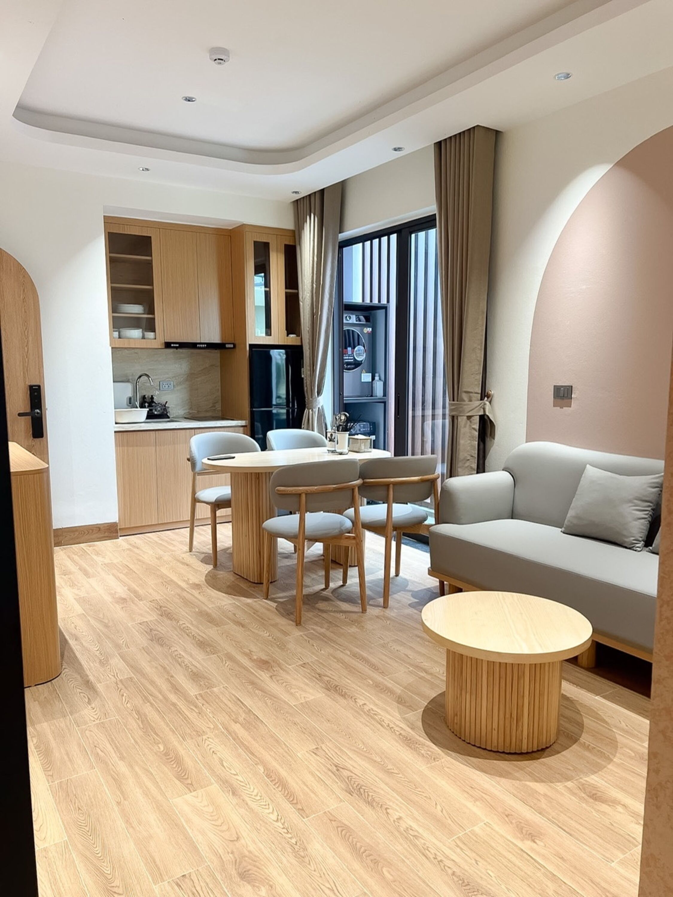 Una sala de estar moderna con un sofá, una mesa de comedor con sillas, una zona de cocina y un ventanal con cortinas.
