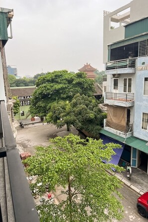 A residential area with a tree in the foreground, a building with a balcony, and a parked red car. - Mina Building Self Check-in Hoa Lu Old Town (Ninh Binh)