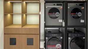A laundry room with stacked washing machines and a wooden shelving unit.