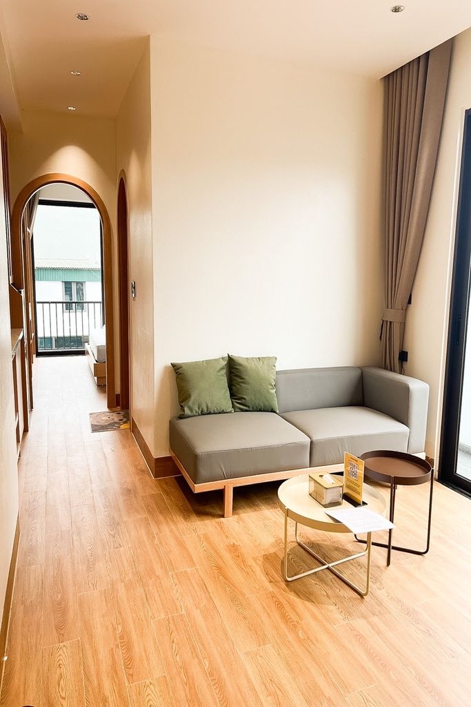 Una sala moderna con un sofá, una mesita redonda y vistas a un balcón a través de una puerta abierta.