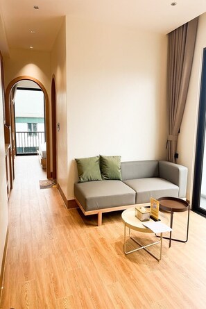 A modern living room with a sofa, a small round table, and a view through an open door to a balcony. - Mina Building Self Check-in Hoa Lu Old Town (Ninh Binh)