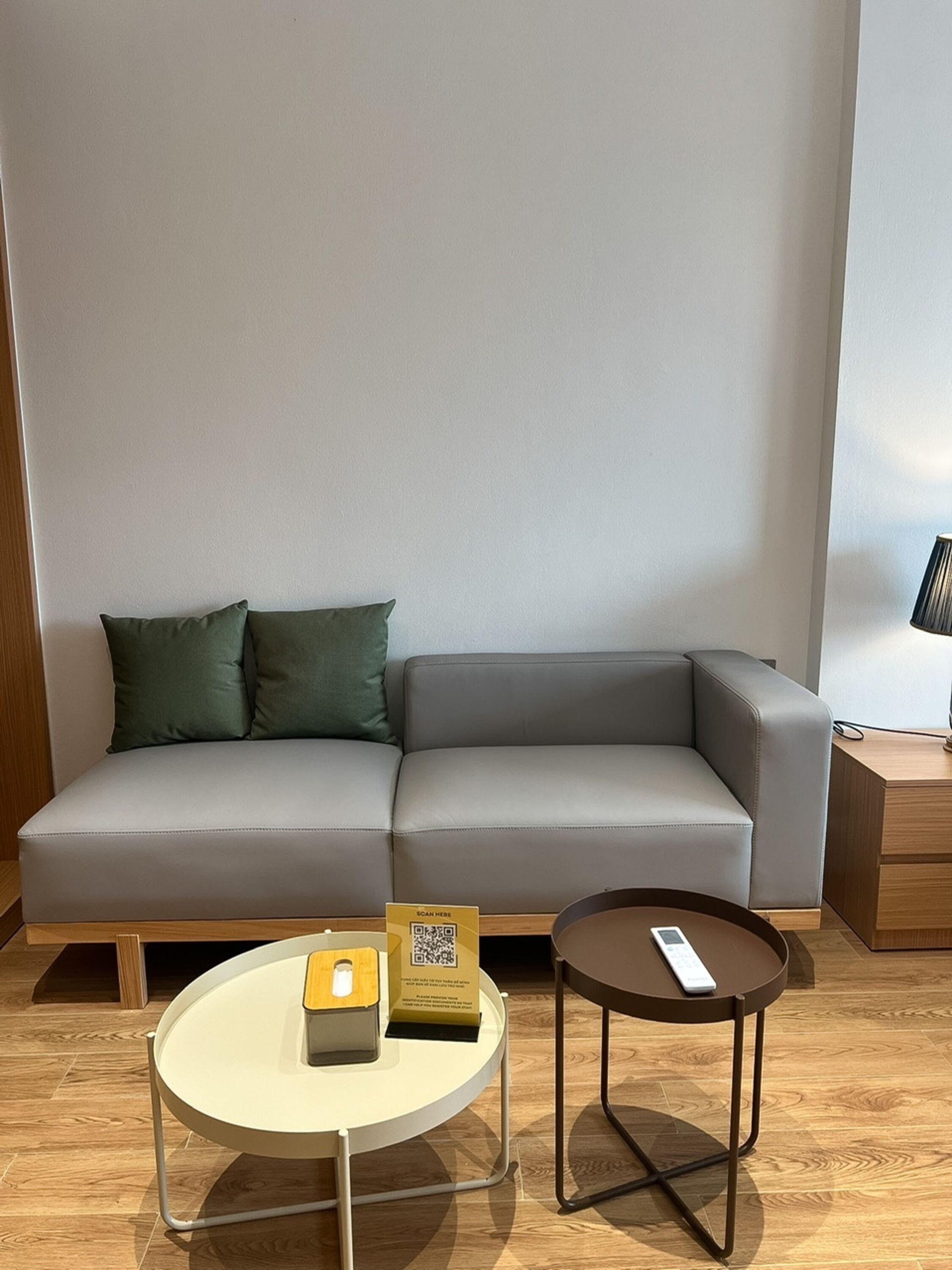 En moderne stue med en grå sofa, et lille rundt bord med en fjernbetjening og en QR-kode på en æske.