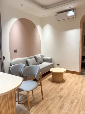 A modern living room with a sofa, two chairs, a round coffee table, wooden flooring, and an air conditioning unit.