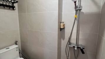 A bathroom with a toilet, a shower with a handheld showerhead, and a towel rack.