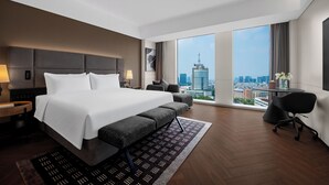 A modern hotel room with a large bed, a desk, a chair, and a view of the cityscape.
