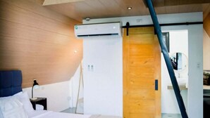 Un dormitorio con cama, mesita de noche, lámpara, puerta de madera y una escalera.