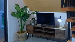 Una sala de estar moderna con una escalera de madera, un televisor de pantalla plana, una planta en maceta y un escritorio con lámpara.