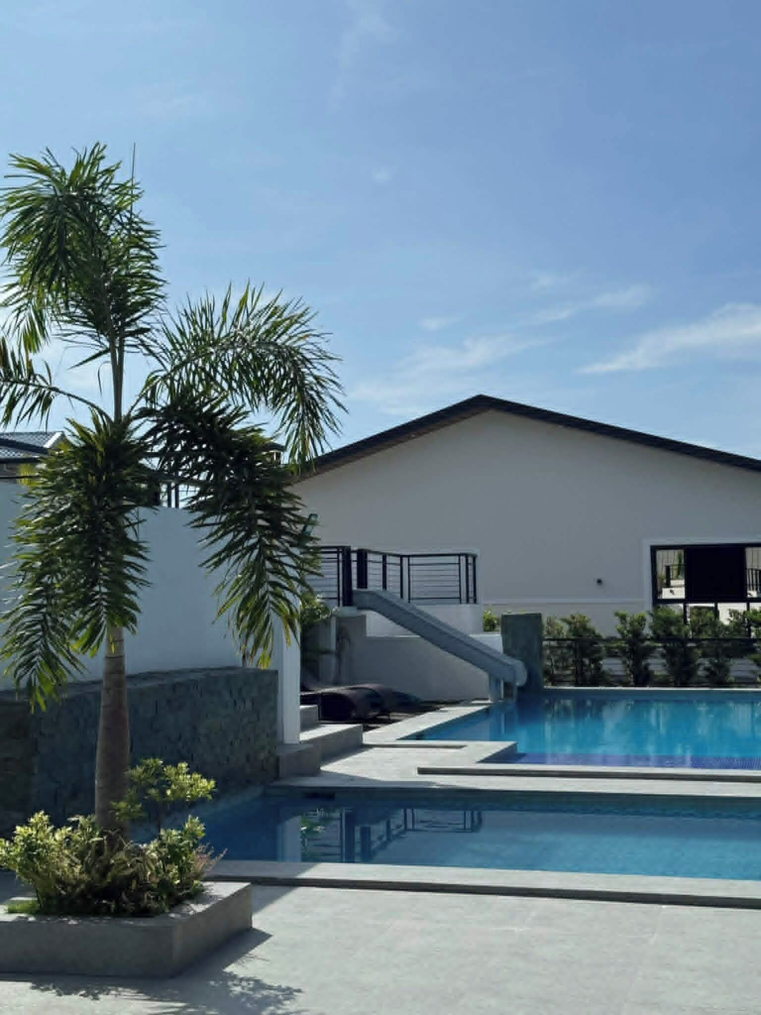 Ein modernes Gebäude mit Swimmingpool, Palmen und einer Treppe, die zu einem Balkon führt.