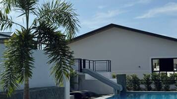 Ein modernes Gebäude mit Swimmingpool, Palmen und einer Treppe, die zu einem Balkon führt.