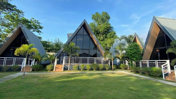 Un edificio moderno con techos triangulares y ventanas amplias, rodeado de un césped cuidado y árboles.
