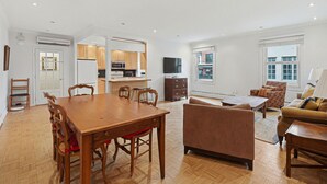 Uma sala de estar ampla com uma mesa de jantar de madeira, um sofá e uma televisão.
