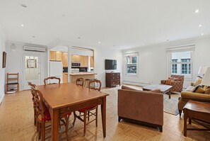 A spacious living area with a wooden dining table, a sofa, and a TV.