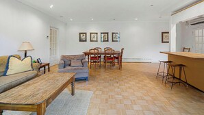 Uma sala de estar com sofá, mesa de centro, mesa de jantar com cadeiras e uma cozinha com banquetas.