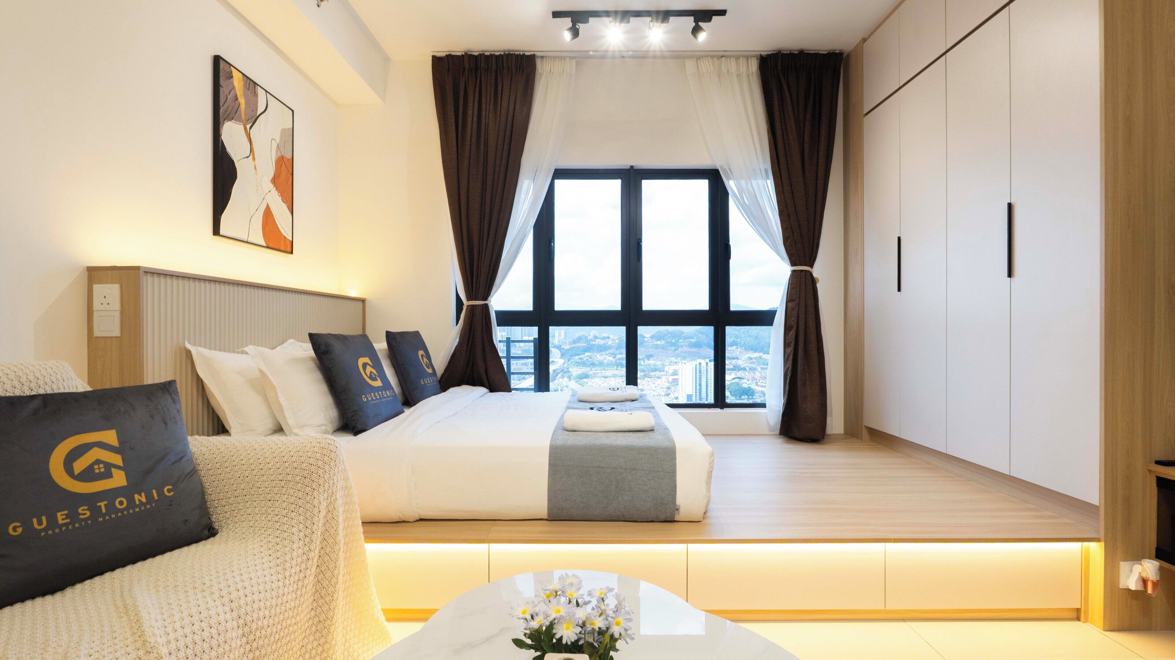 Moderni hotellihuone, jossa on suuri sänky, näköala kaupunkiin sekä työpöytä ja tuoli.