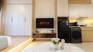 Una cocina moderna con microondas integrado, refrigerador negro y televisor de pantalla plana sobre un mueble de madera.