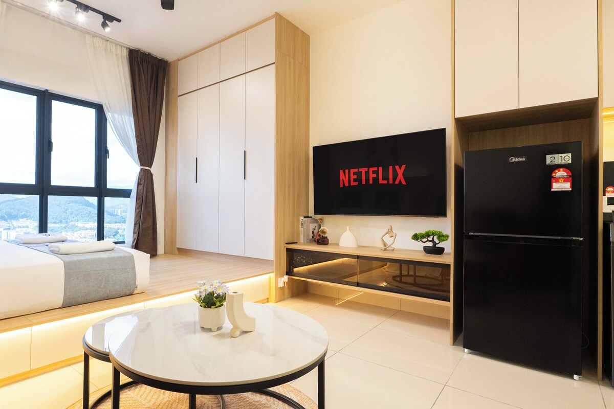 A modern hotel room with a bed, a small table, a TV, and a refrigerator.