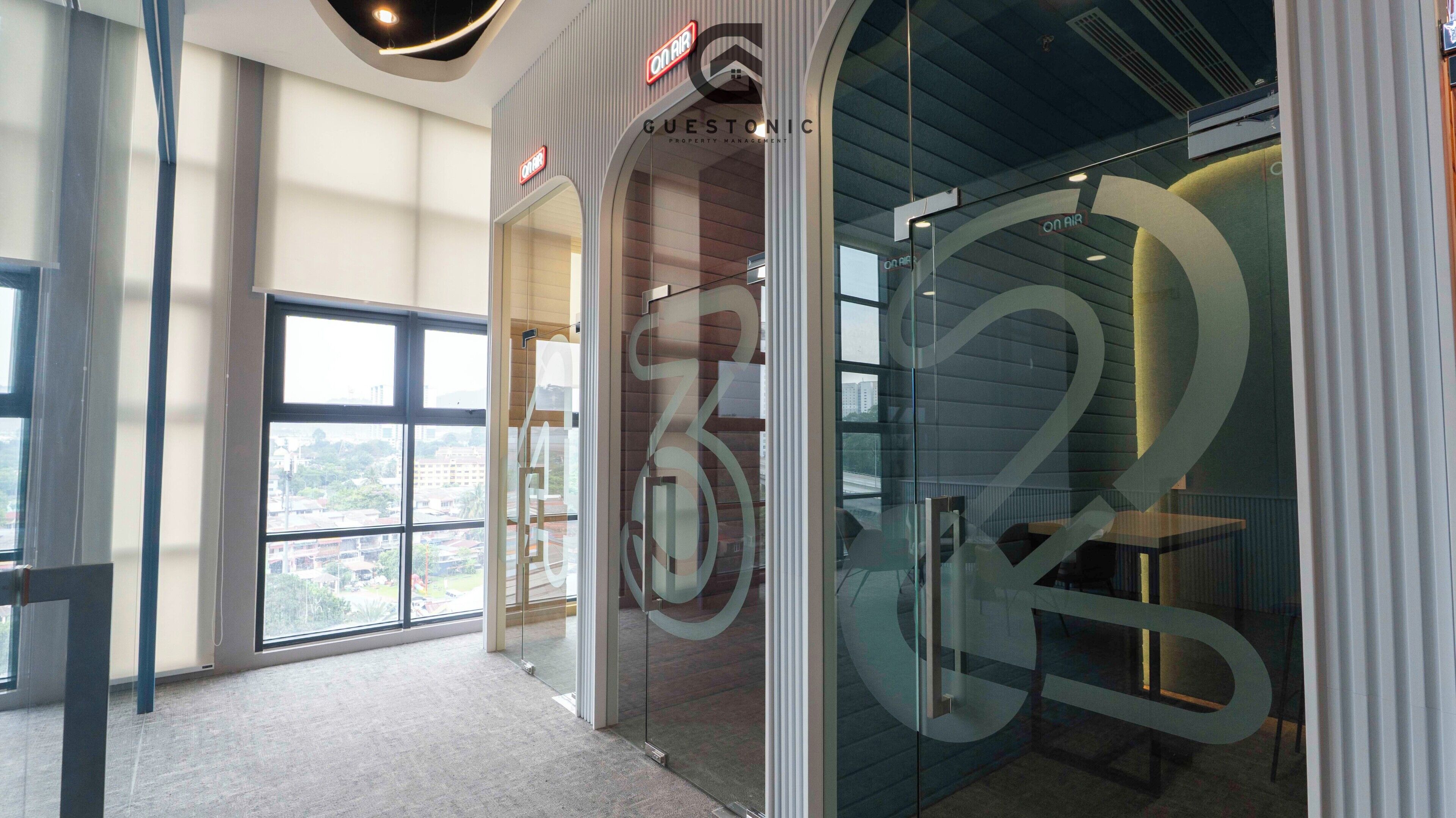 A modern interior with large windows, a glass wall with a circular design, and a sign for 'On Air Guestonic Property Management'.