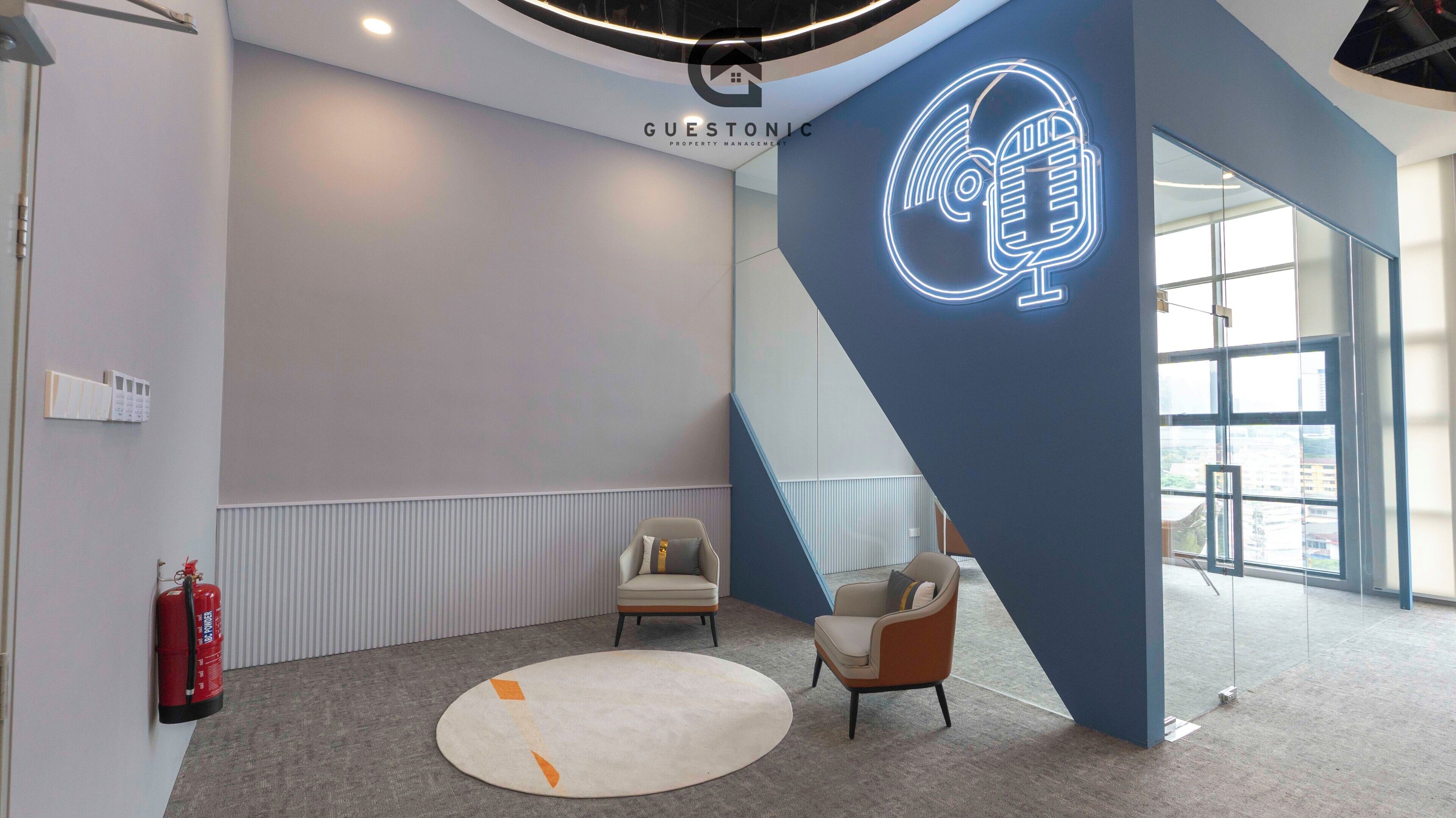 Een modern interieur met een neonbord in de vorm van een microfoon, een brandblusser en twee stoelen.