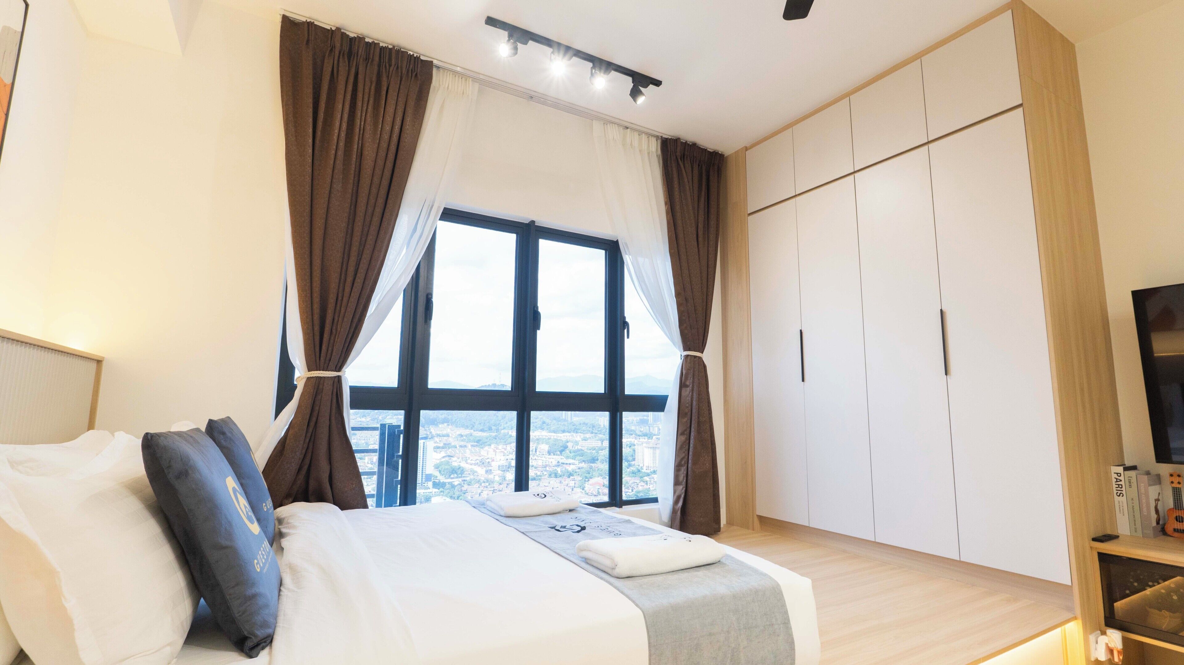 A hotel room with a large bed, a view of the city through a window, and a wardrobe with multiple compartments.