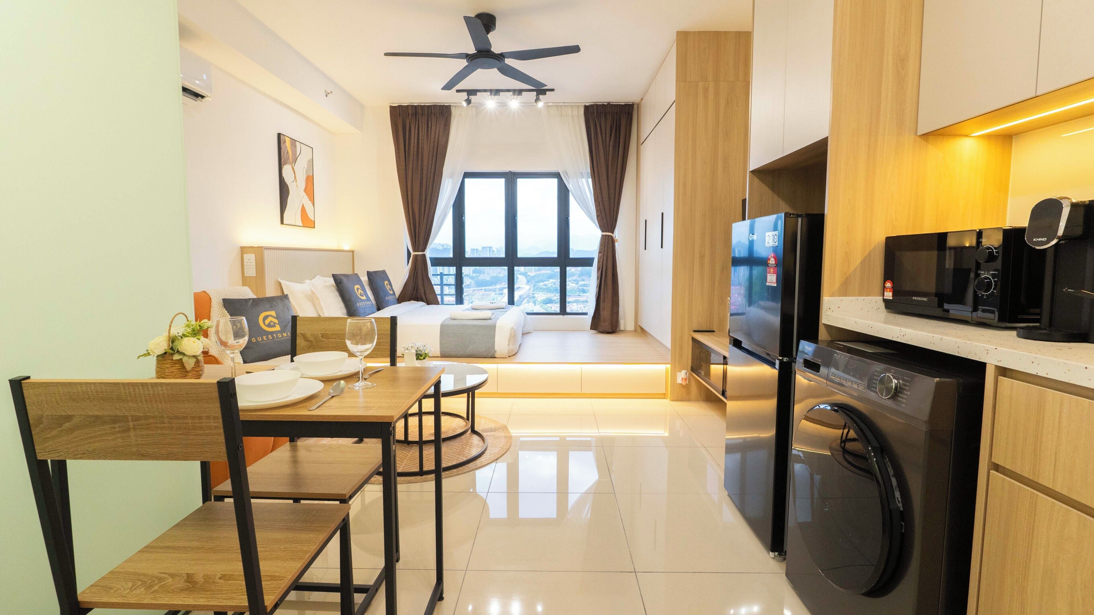 Una habitación de hotel moderna con comedor, kitchenette y un amplio ventanal con cortinas.