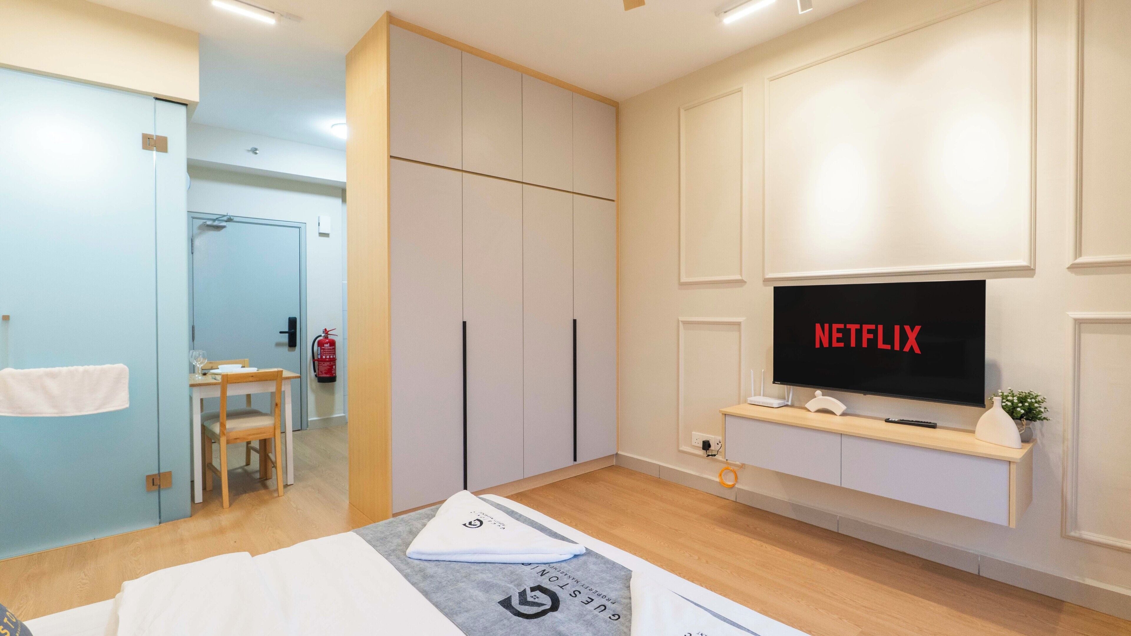 A modern hotel room with a bed, a TV mounted on the wall, a small table, and a chair.