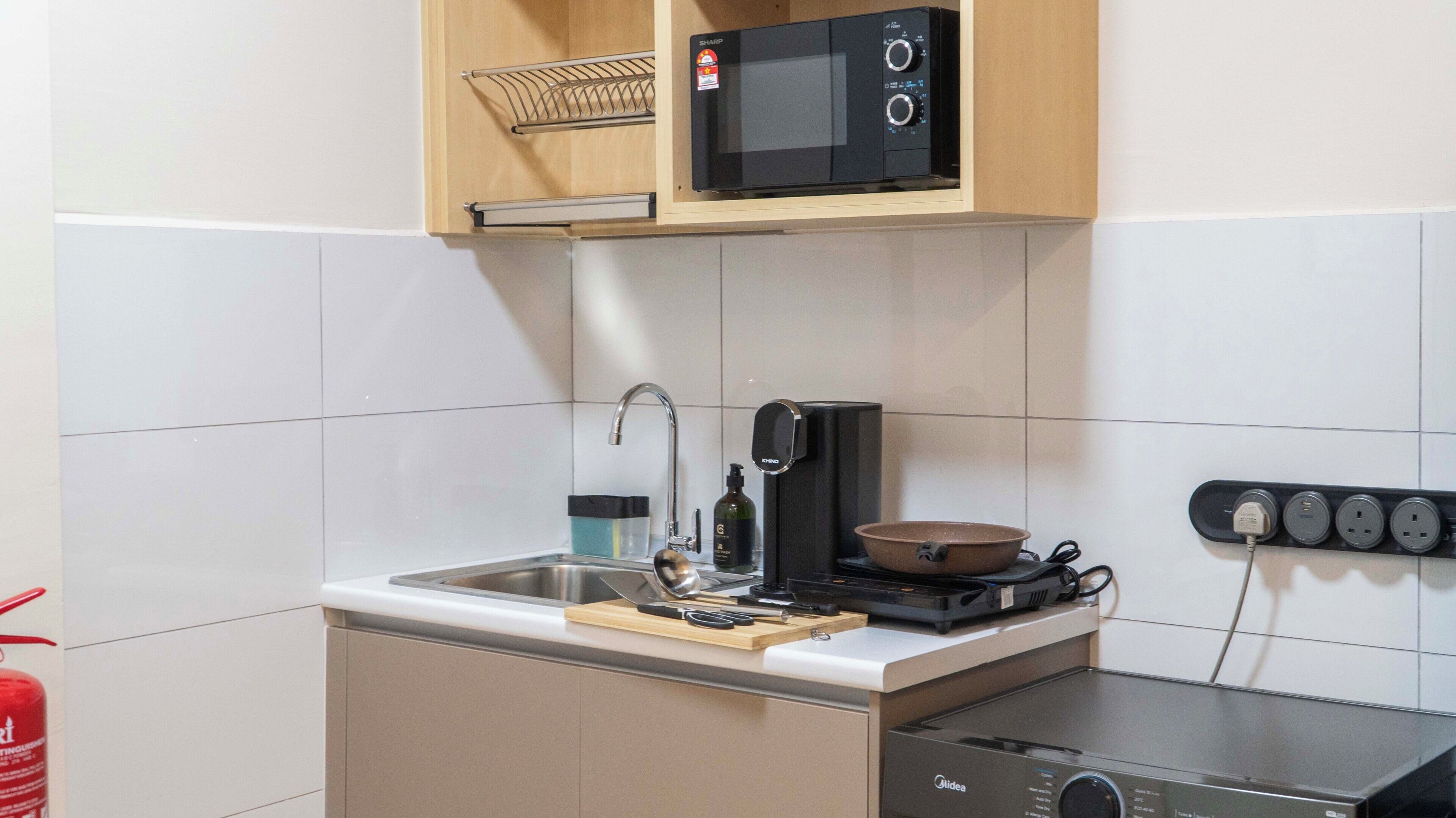 Una cocina compacta con microondas, estufa, lavaplatos y una regleta de enchufes.