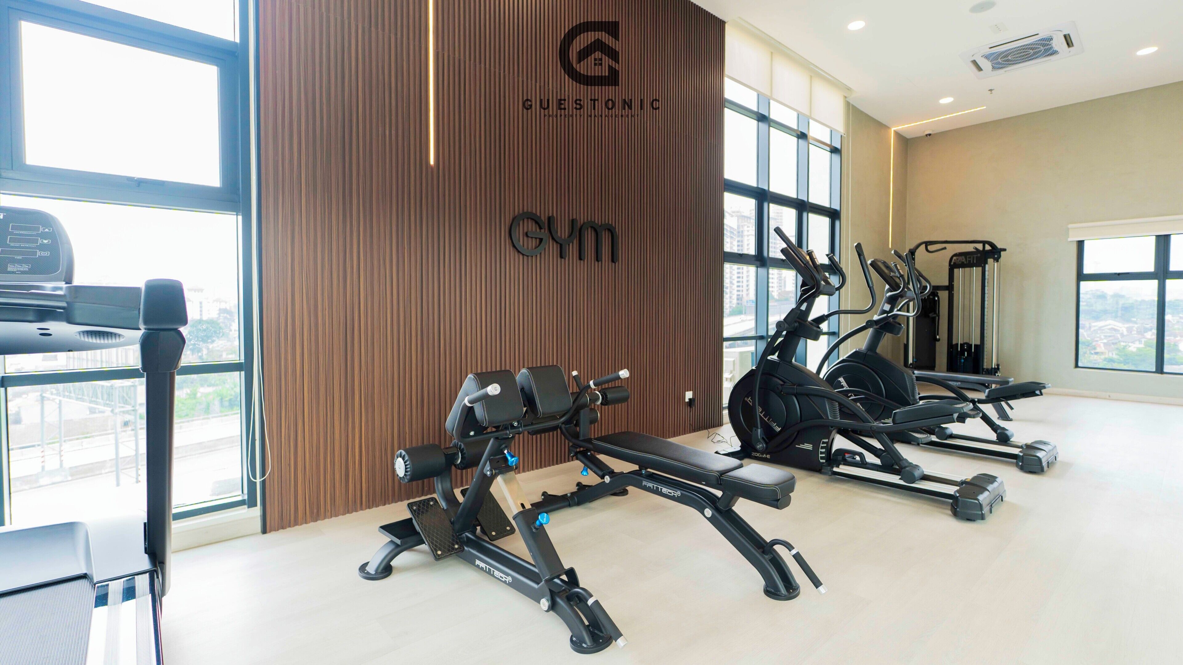 Un gimnasio con equipo de ejercicio, una pared de madera con un logotipo y ventanas grandes.