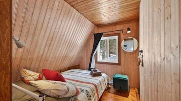 Une chambre dans une cabane en bois, avec un lit superposé, une petite table, un miroir et une fenêtre avec des rideaux.