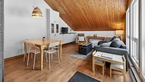 Une pièce de style « loft », avec un plafond en bois, un coin repas comprenant une table et des chaises en bois, un canapé et un téléviseur en arrière-plan.