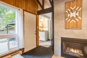 A wooden interior with a fireplace, a door leading to a kitchen, and a view of the outdoors. - La Petite Echappee - spa (Orford)
