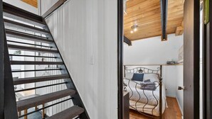 Un escalier menant à une chambre à coucher avec un lit, un plafond en bois et un mur blanc.