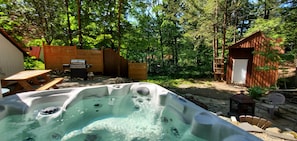 A hot tub in a forested backyard with a wooden deck, picnic table, and barbecue grill. - La Petite Echappee - spa (Orford)