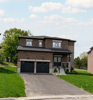 Une maison à deux étages avec une façade en briques, deux portes de garage, un porche à l’avant et une allée.