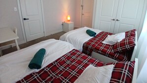 A room with two beds, white walls, and a small table with a lamp.