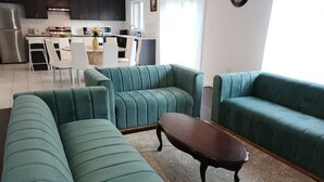 A living room with teal sofas, a coffee table, and a kitchen in the background.